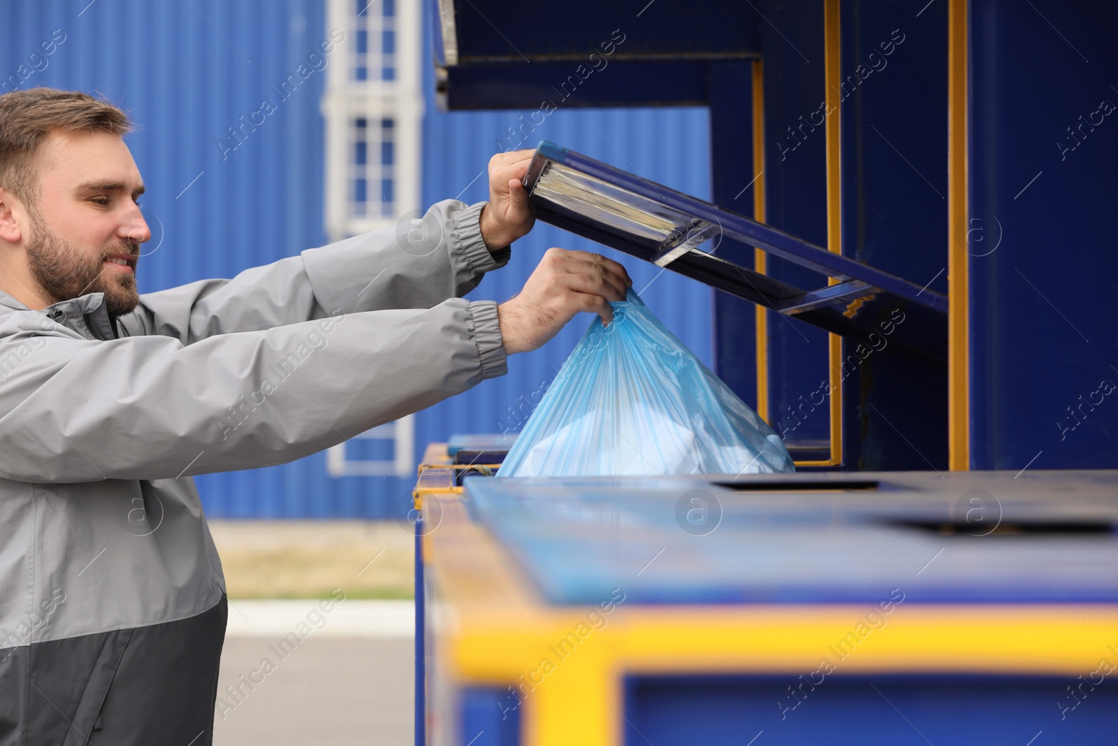 Photo of Man throwing garbage into bin at recycling point outdoors