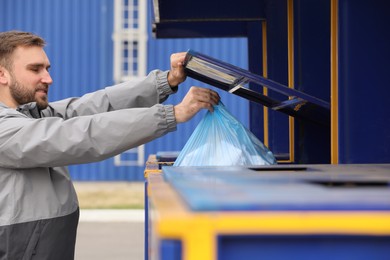 Photo of Man throwing garbage into bin at recycling point outdoors