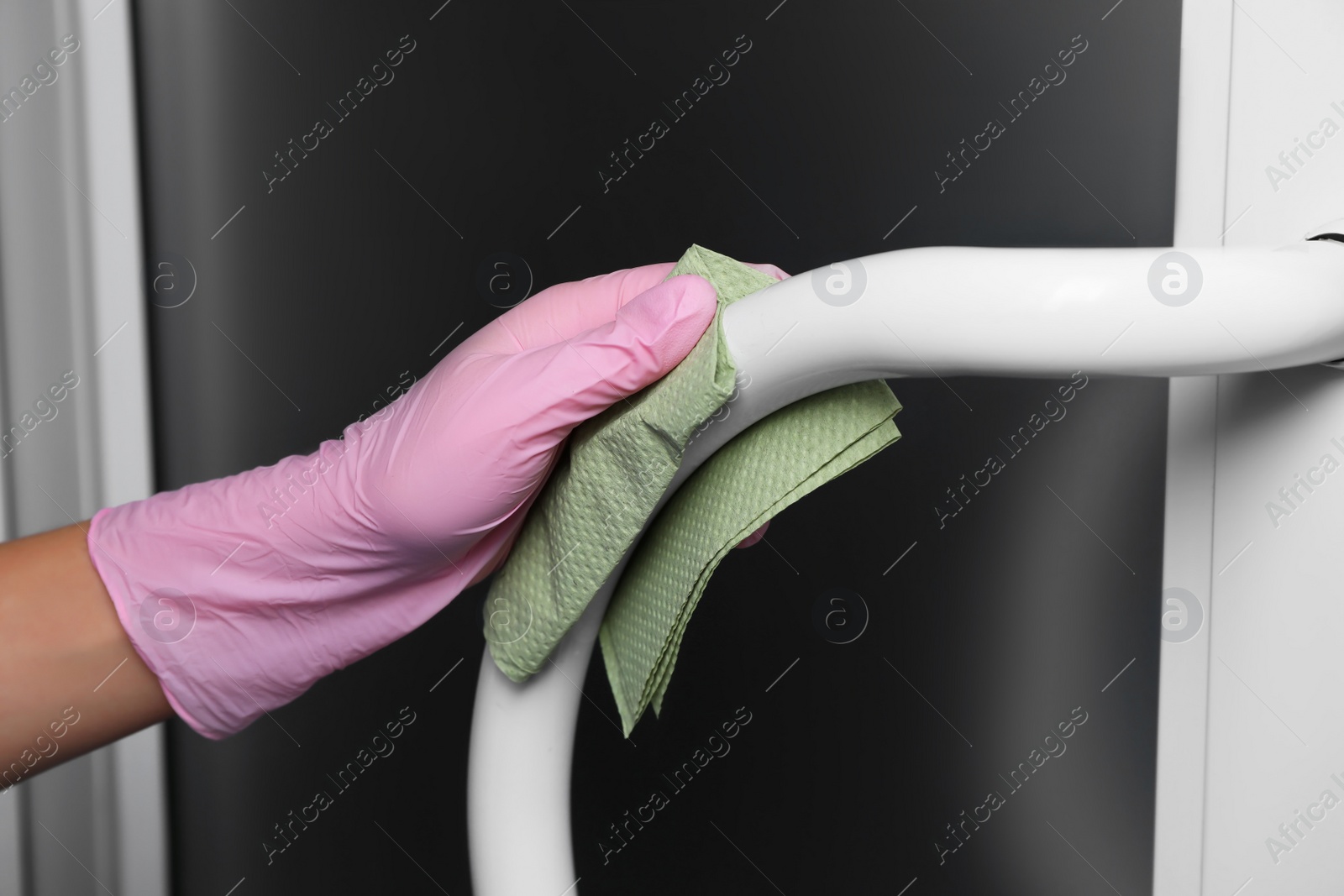 Photo of Woman in glove cleaning door handle with paper towel indoors, closeup