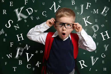 Image of Funny little child with glasses and letters near chalkboard. Speech therapy concept