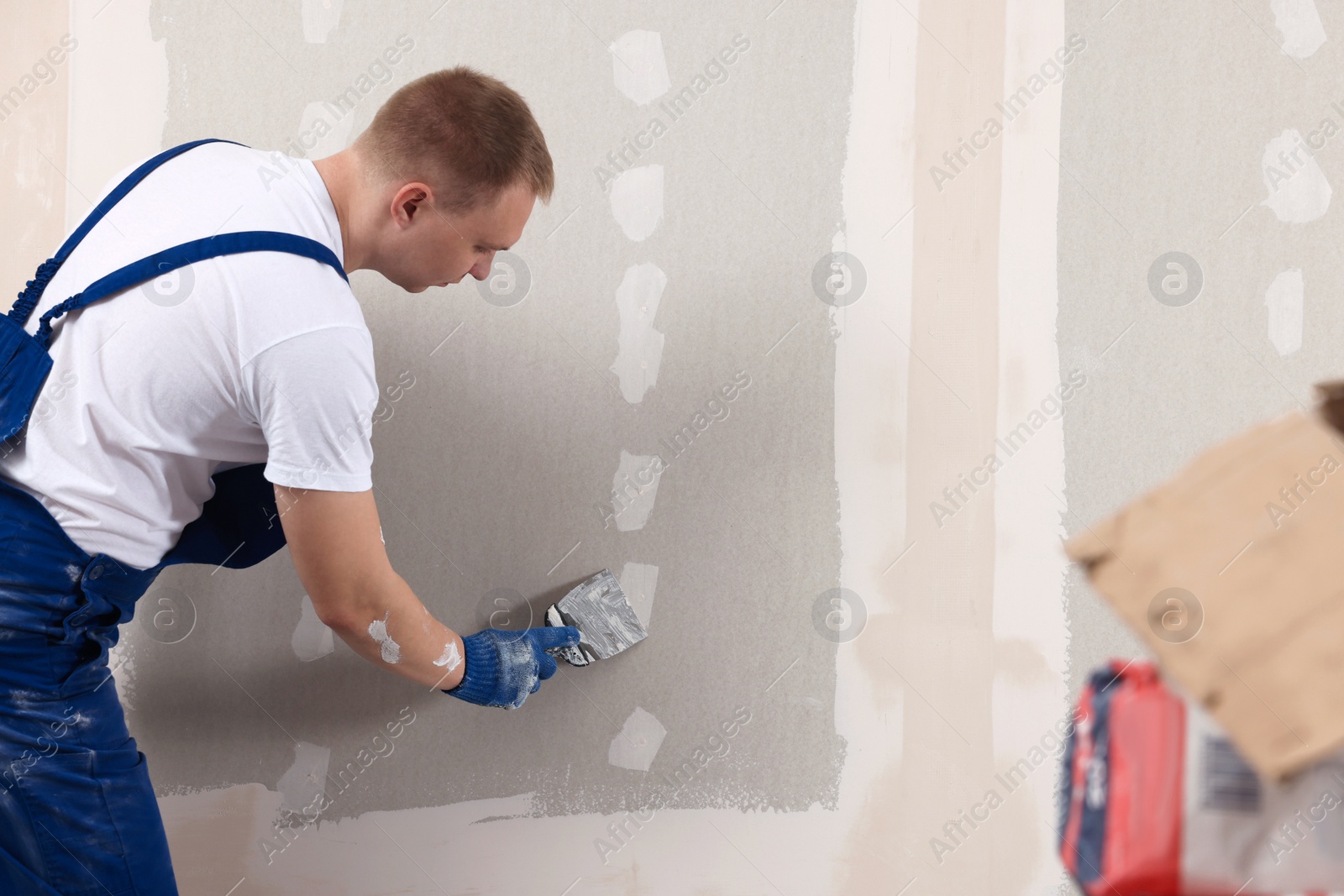 Photo of Man plastering wall with putty knife indoors. Home renovation