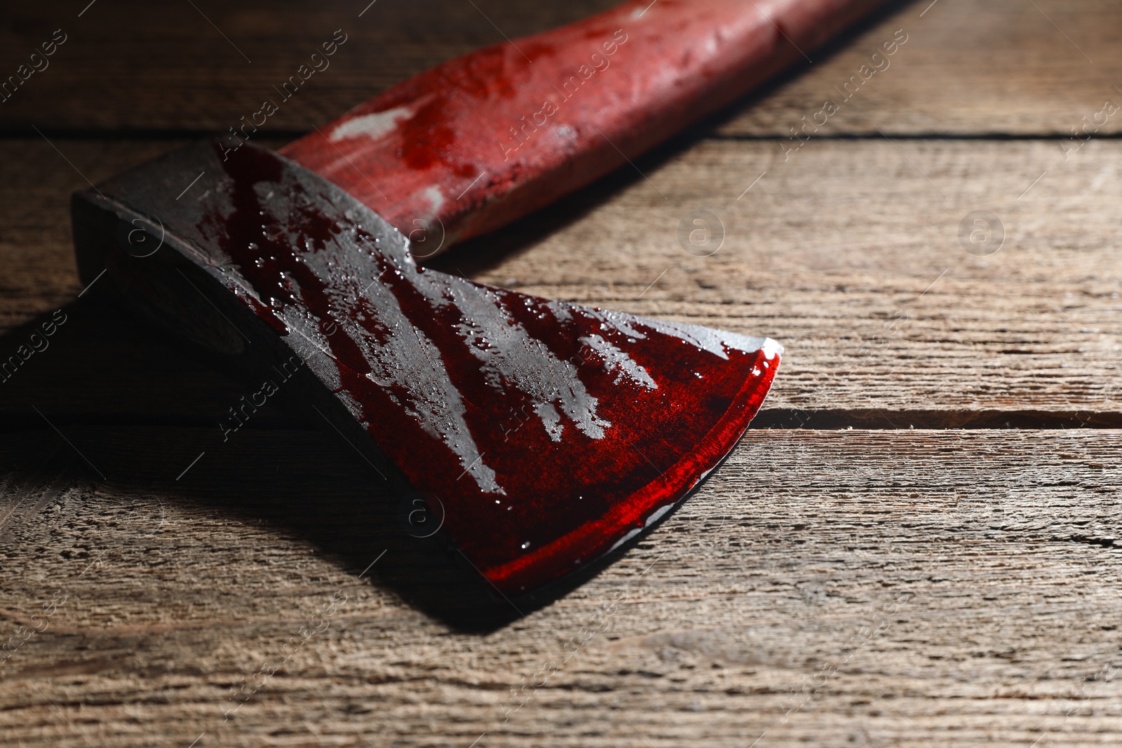 Photo of Axe with blood on wooden surface, closeup