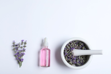 Bottle of essential oil, mortar and pestle with lavender flowers on white background, flat lay