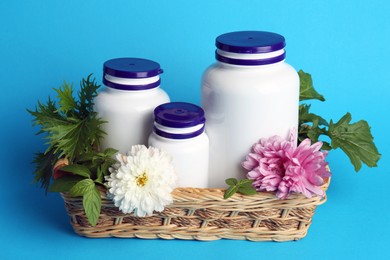 Photo of White medical bottles, arugula and flowers in wicker tray on light blue background