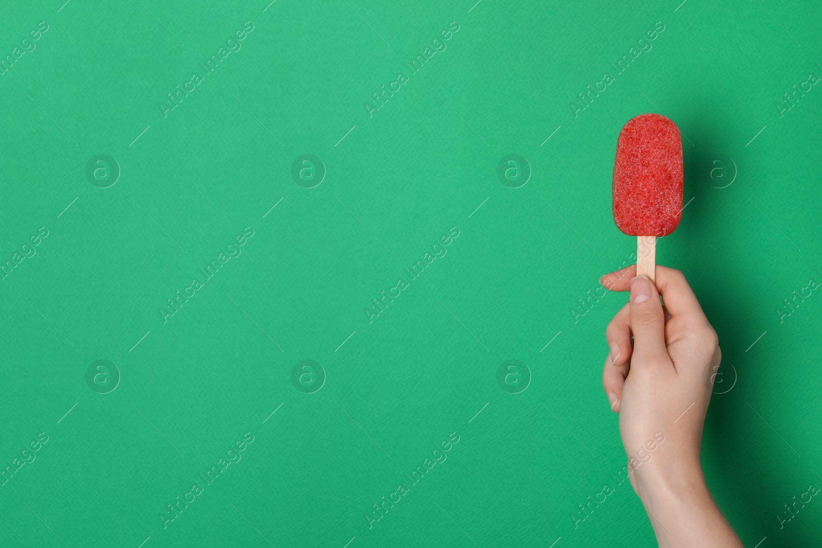 Photo of Woman holding tasty fruit ice pop on green background, space for text