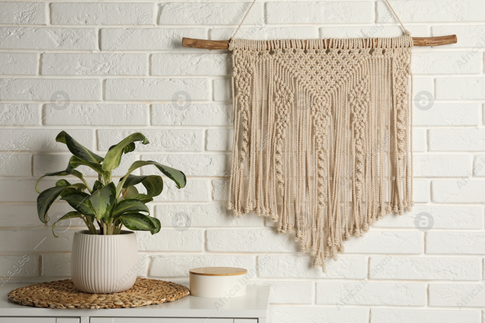 Photo of Beautiful macrame hanging on white brick wall in room. Decorative element