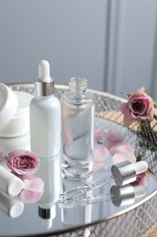 Photo of Bottles of cosmetic serum and beautiful flowers on table