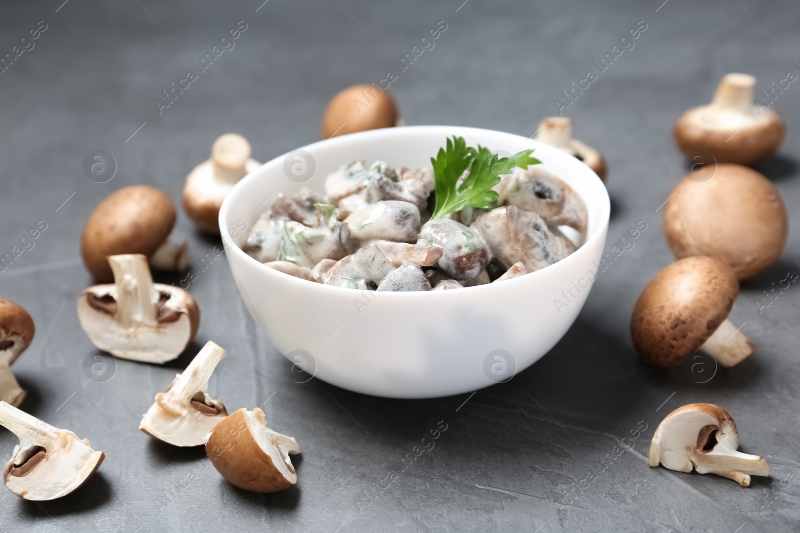 Photo of Bowl of fried mushrooms with sauce on grey table