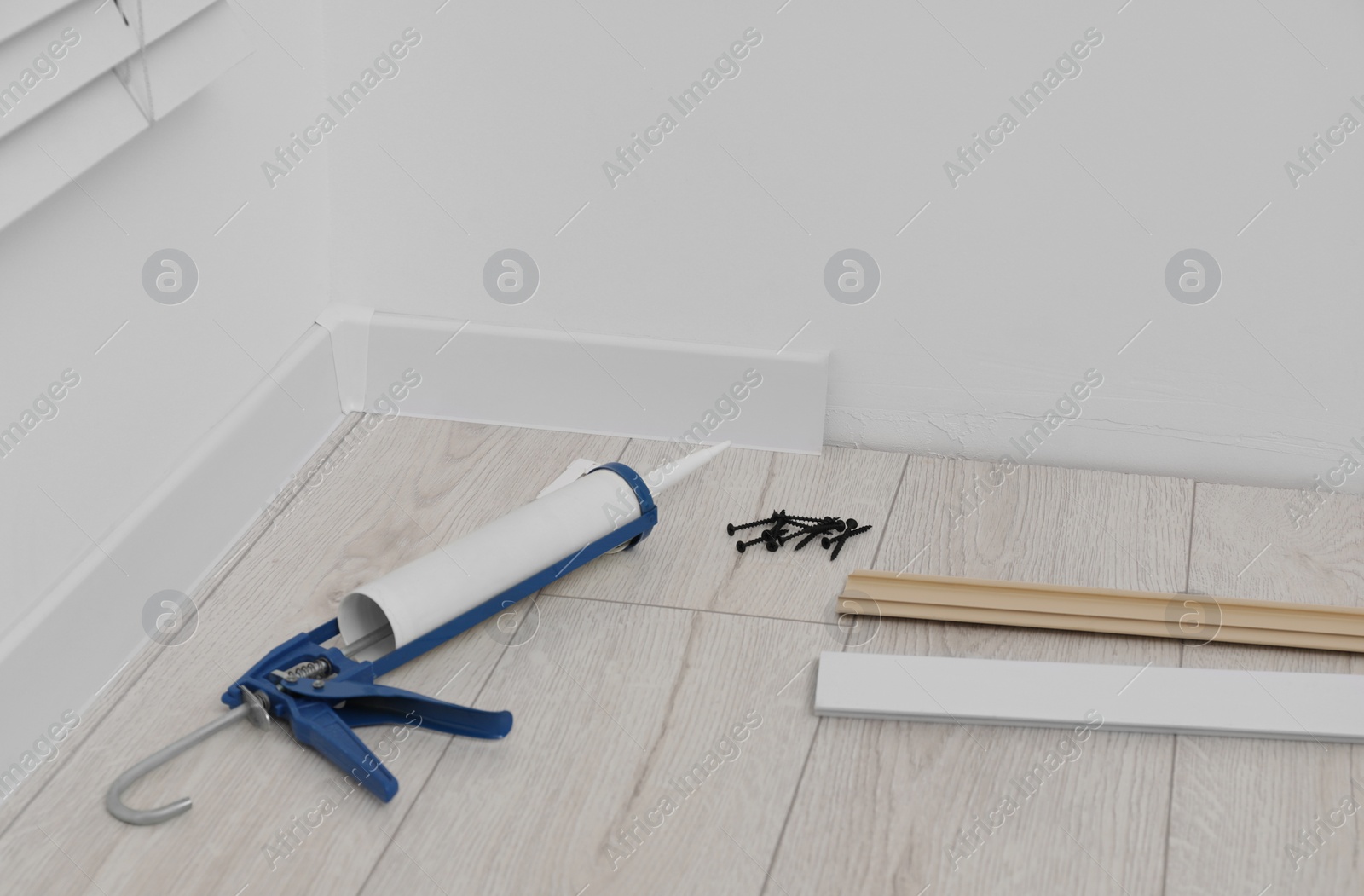 Photo of Plinths, caulking gun and screws on laminated floor in room