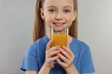 Cute little girl with glass of fresh juice on light gray background