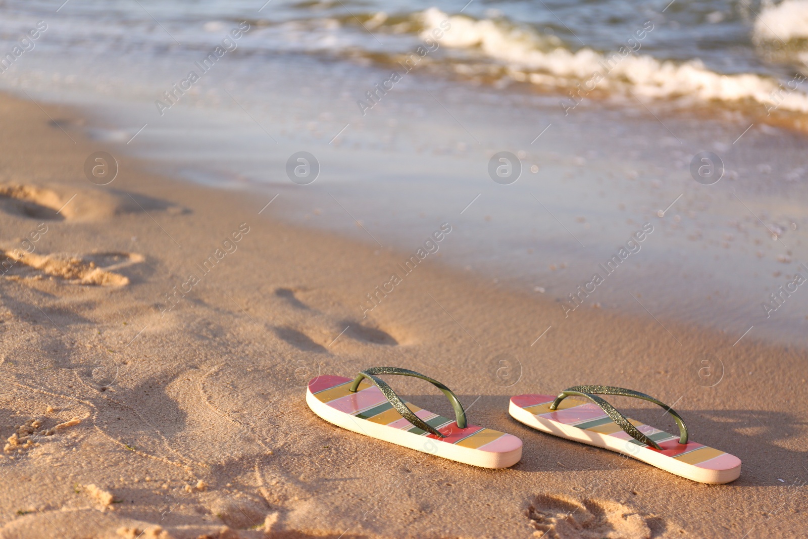 Photo of Stylish flip flops on sand near sea, space for text. Beach accessories