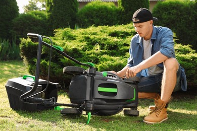 Photo of Young man with screwdriver fixing lawn mower in garden on sunny day