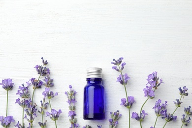 Photo of Bottle with natural essential oil and lavender flowers on white wooden background, flat lay. Space for text