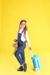 Cute little girl with suitcase on yellow background