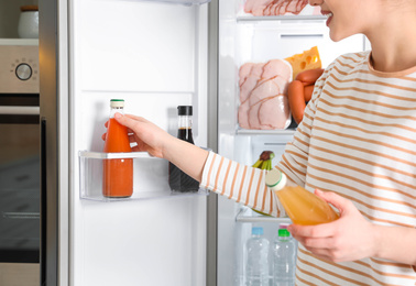 Photo of Young woman taking juice out of refrigerator indoors, closeup