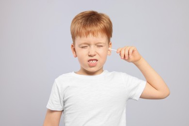 Photo of Little boy cleaning ear with cotton swab on light grey background