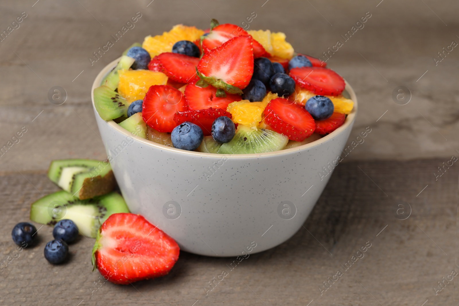 Photo of Delicious fresh fruit salad in bowl and ingredients on wooden table, closeup