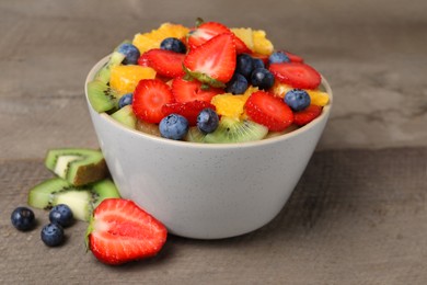 Delicious fresh fruit salad in bowl and ingredients on wooden table, closeup