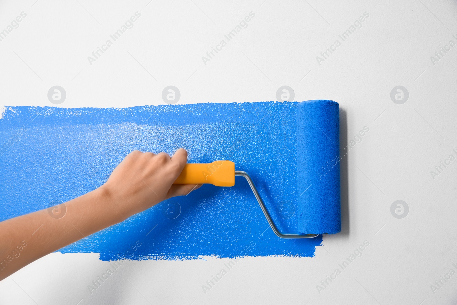 Photo of Woman painting white wall with blue dye, closeup. Interior renovation