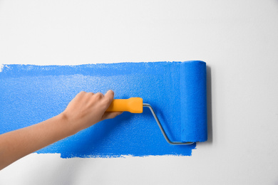 Photo of Woman painting white wall with blue dye, closeup. Interior renovation