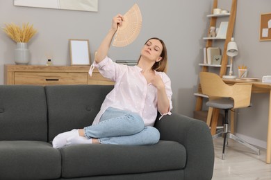 Photo of Woman waving hand fan to cool herself on sofa at home