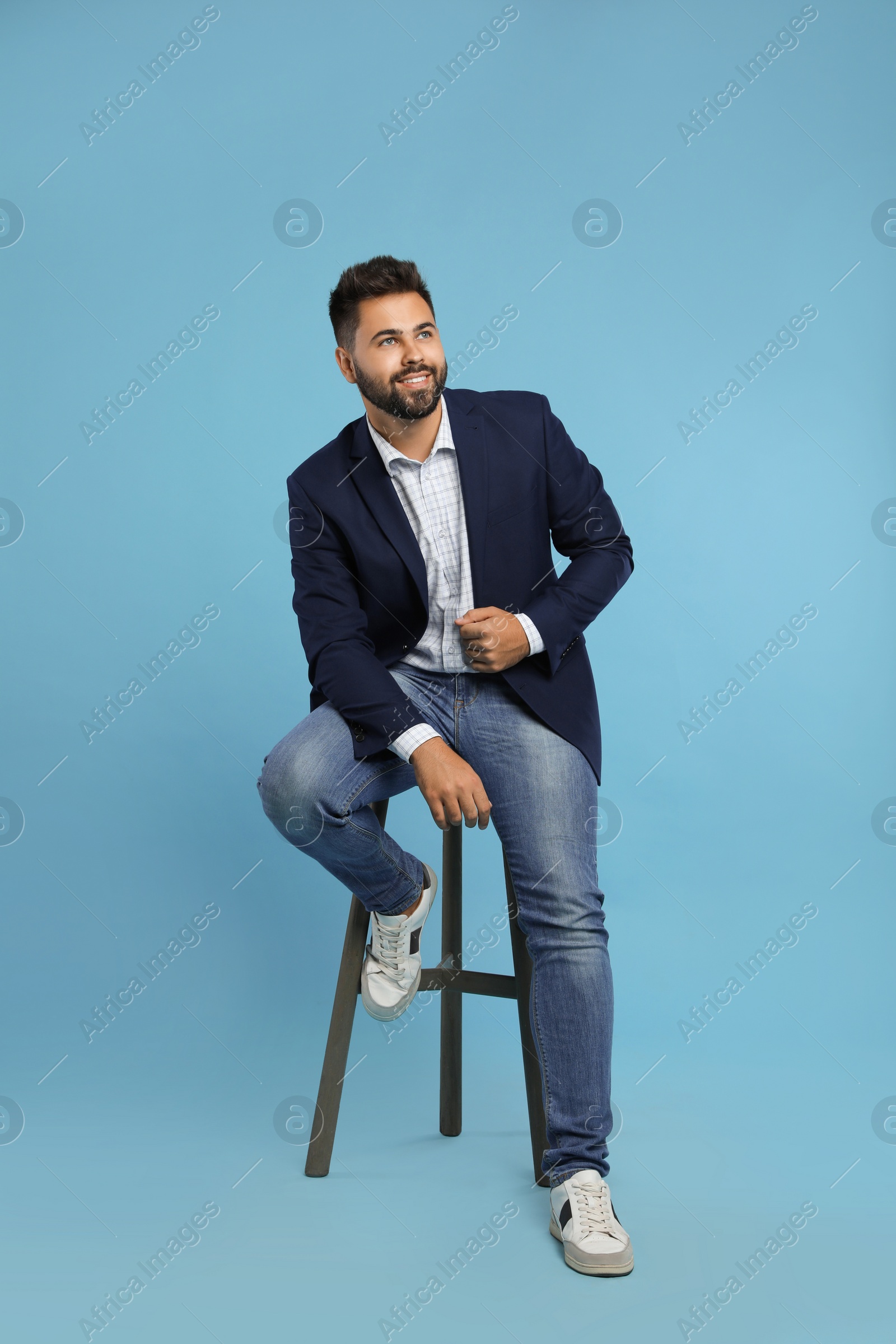 Photo of Handsome young man sitting on stool against turquoise background