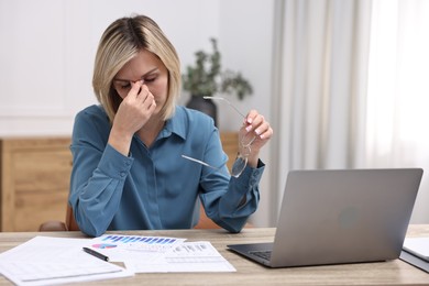 Overwhelmed woman with glasses sitting at table in office