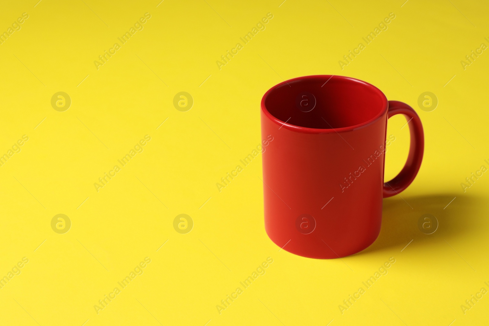 One red ceramic mug on yellow background, space for text Photo of One red ceramic mug on yellow background, space for text
