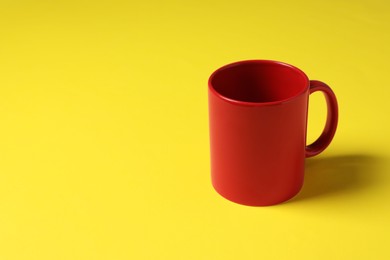 Photo of One red ceramic mug on yellow background, space for text
