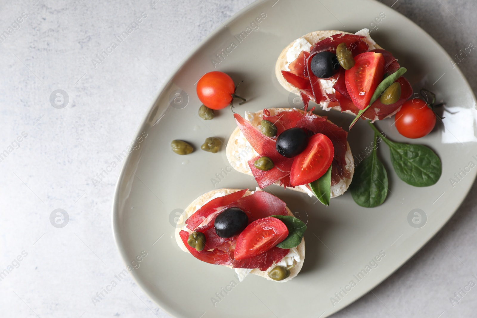 Photo of Delicious sandwiches with bresaola, cream cheese, olives and tomato on light table, top view