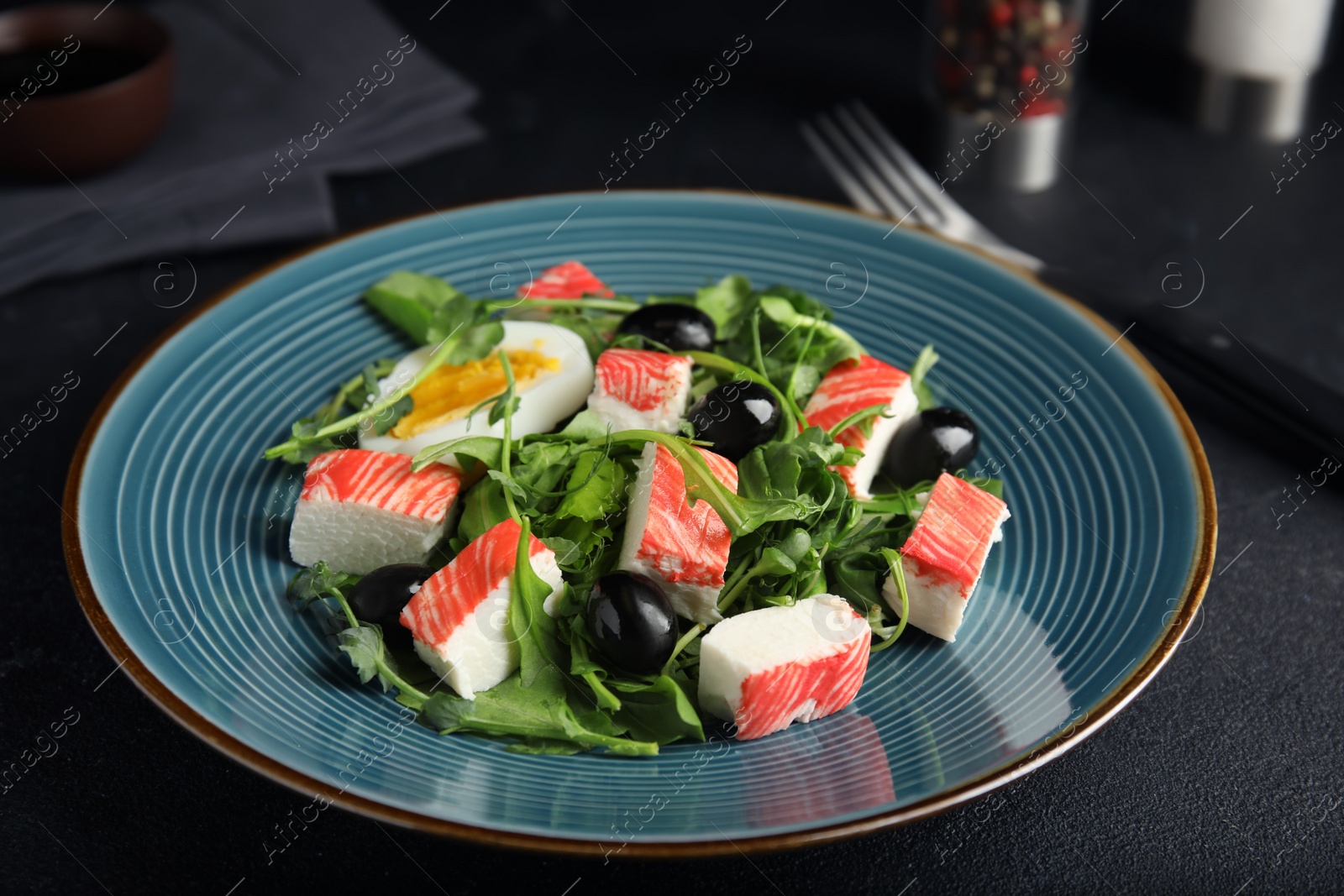 Photo of Delicious crab stick salad served on black table