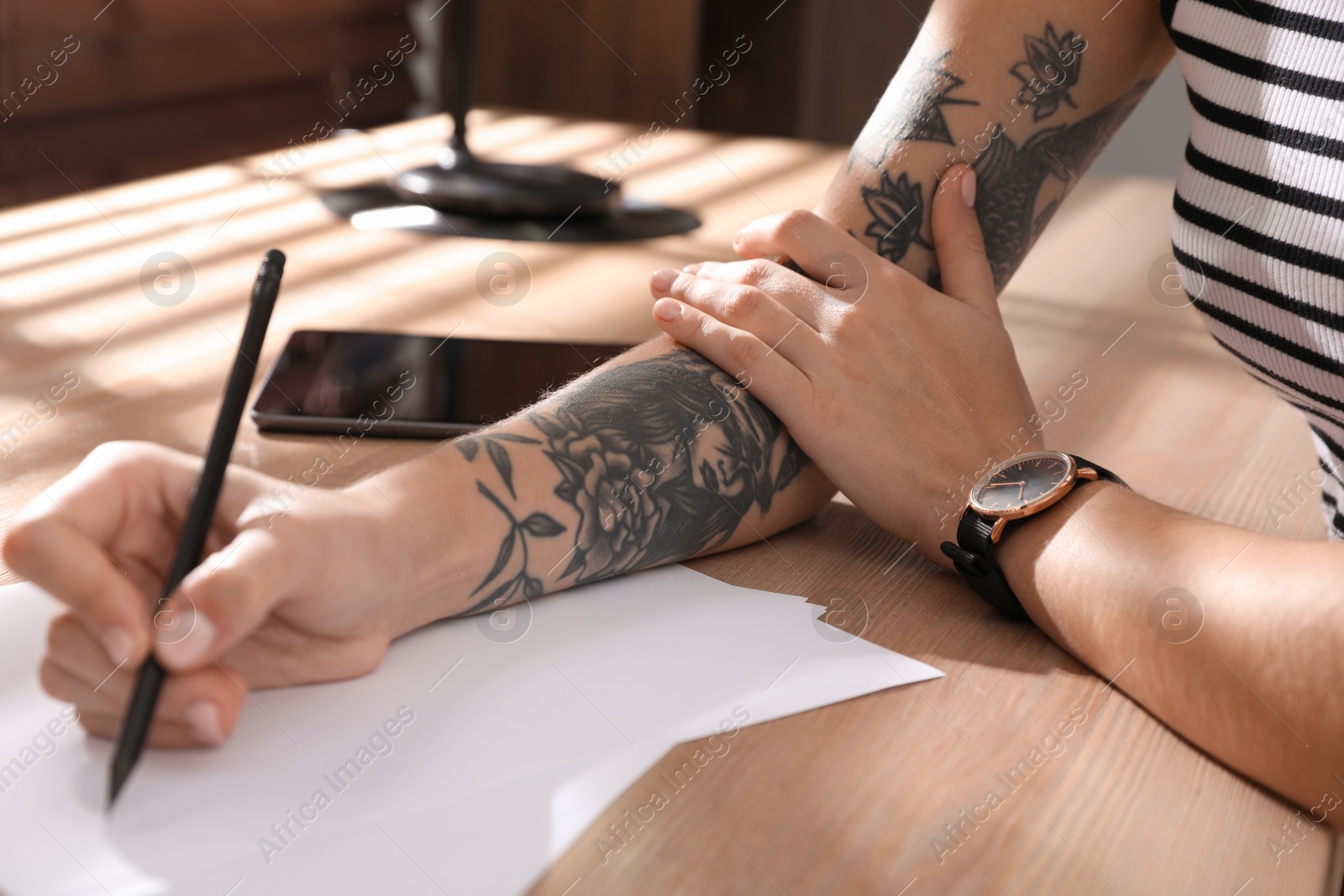 Photo of Woman with tattoos on arm drawing in sketchbook at table, closeup