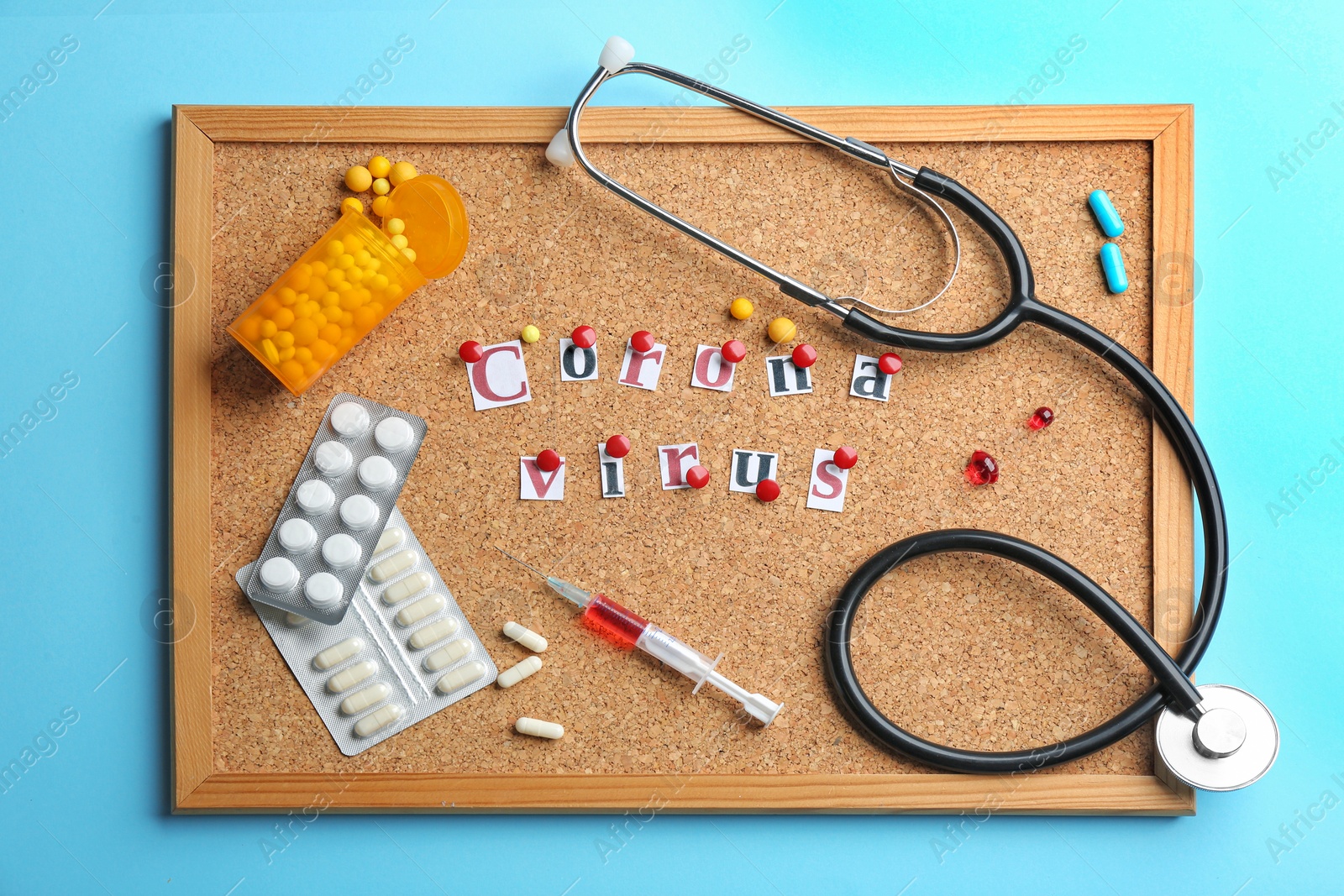 Photo of Corkboard with words CORONA VIRUS and medications on light blue background, flat lay