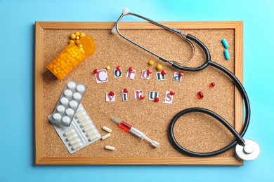 Photo of Corkboard with words CORONA VIRUS and medications on light blue background, flat lay