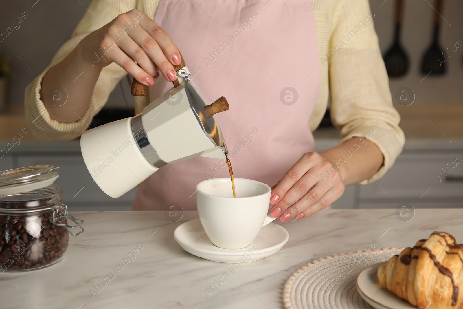 Photo of Woman pouring aromatic coffee from moka pot into cup at white marble table, closeup