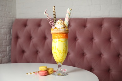 Glass of tasty milk shake with sweets on table indoors
