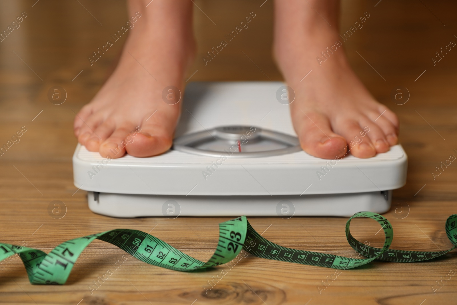 Photo of Overweight girl using scales near measuring tape on wooden floor, closeup