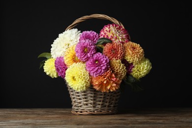 Basket with beautiful dahlia flowers on wooden table against black background