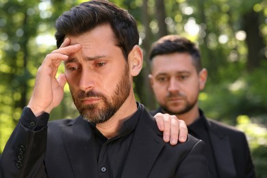 Photo of Funeral ceremony. Man comforting his friend outdoors