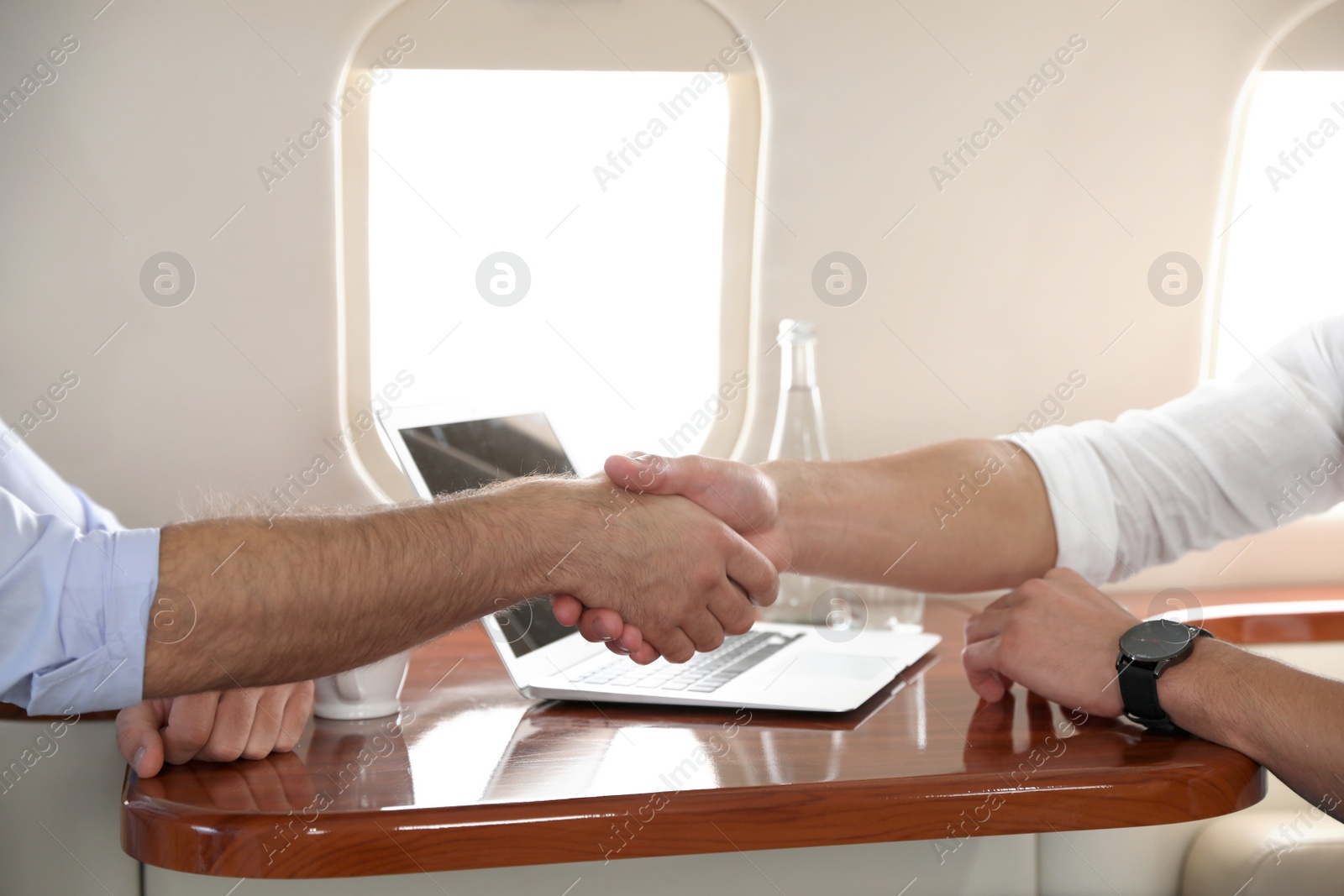 Photo of Young people shaking hands after bargaining on plane, closeup. Business deal