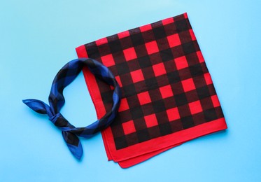 Photo of Tied and folded checkered bandanas on light blue background, flat lay