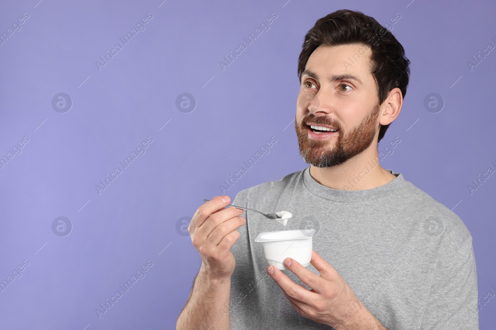 Photo of Handsome man with delicious yogurt and spoon on violet background. Space for text