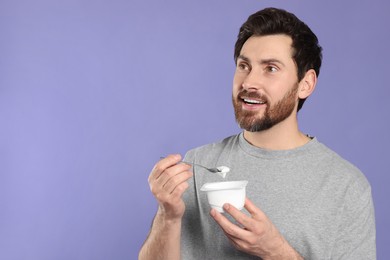 Handsome man with delicious yogurt and spoon on violet background. Space for text
