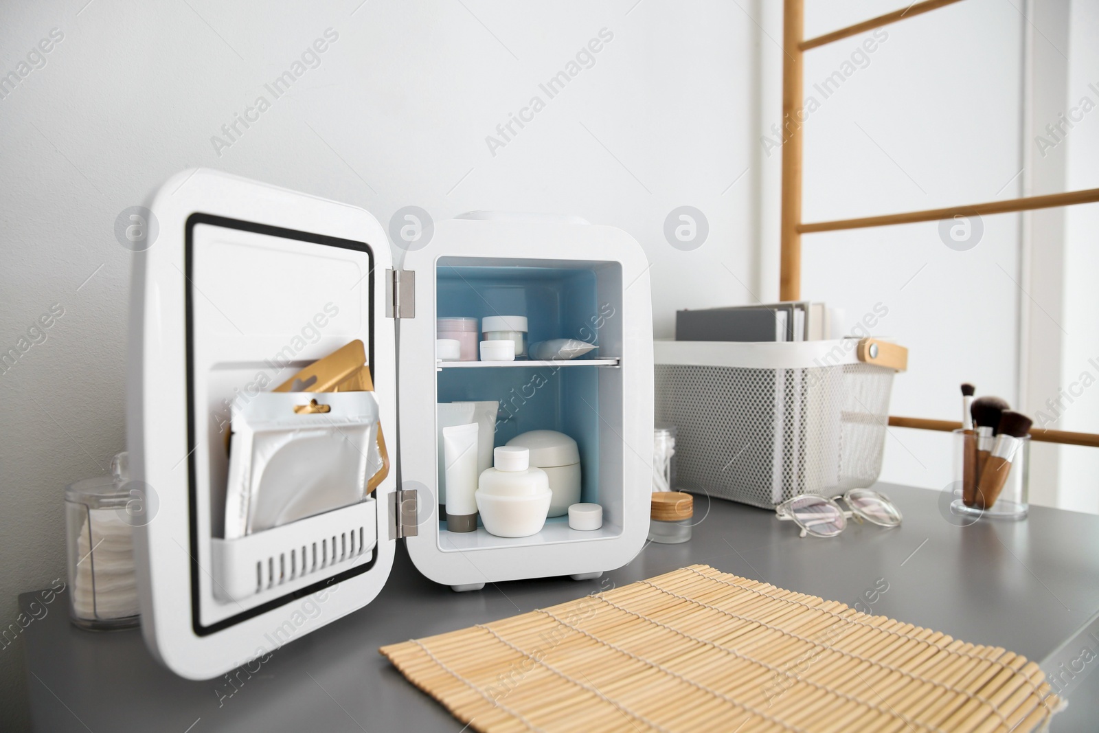 Photo of Mini fridge with cosmetic products on grey vanity table indoors