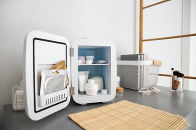 Photo of Mini fridge with cosmetic products on grey vanity table indoors