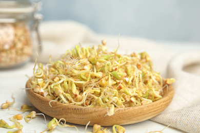 Plate of sprouted green buckwheat on white wooden table, closeup