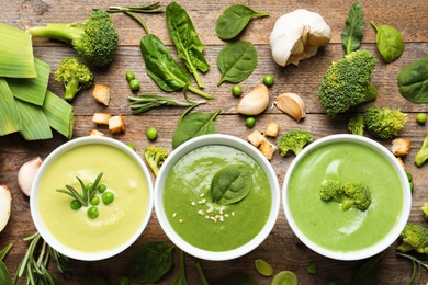 Flat lay composition with different fresh vegetable detox soups made of green peas, broccoli and spinach in dishes on wooden background