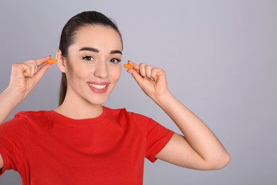 Photo of Young woman inserting foam ear plugs on grey background