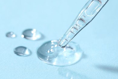 Photo of Glass pipette and transparent liquid on light blue background, closeup