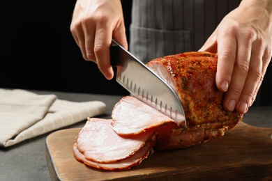 Woman cutting ham on wooden board at table, closeup